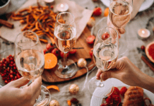 Glasses of champagne being held over a table of holiday food.