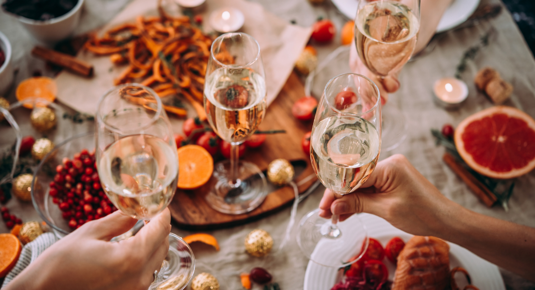 Glasses of champagne being held over a table of holiday food. 