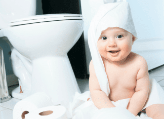 A baby wrapped in toilet paper sitting next to a toilet.