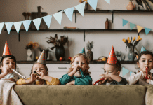 Kids standing behind a couch with party hats and blowers.