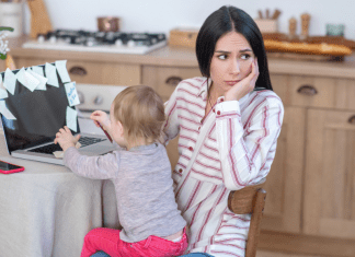 A mother sitting at the computer with a toddler in her lap.
