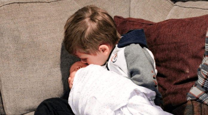 A big brother kissing his baby sister.
