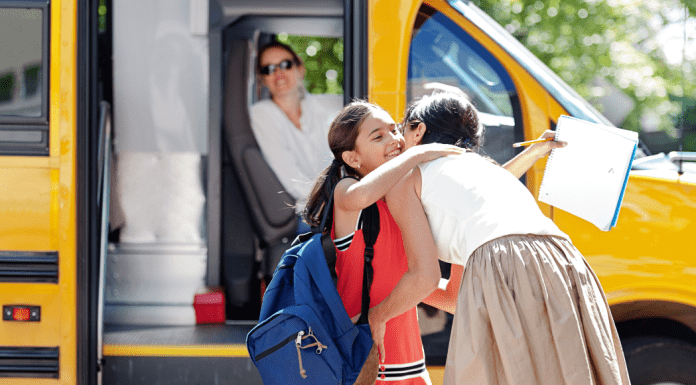 A mom hugging her daughter before she gets on the school bus.