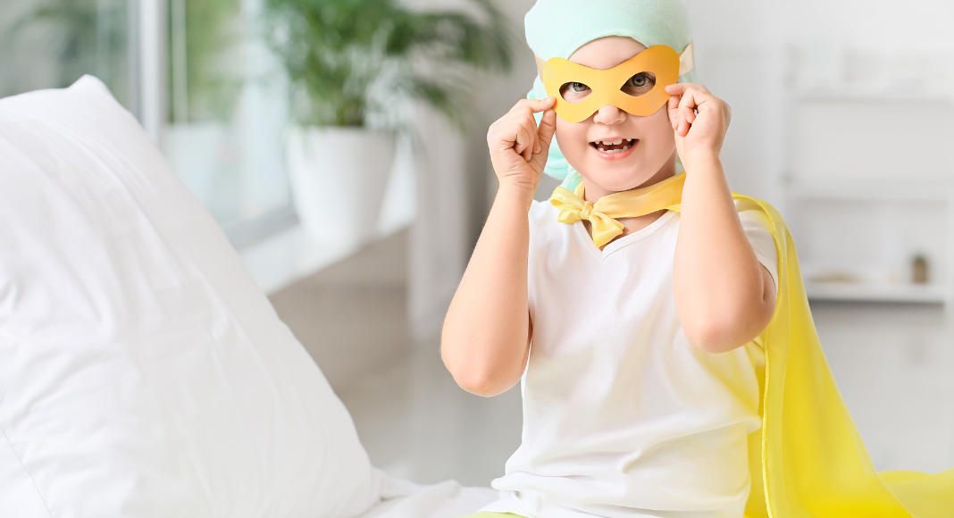 A child with cancer dressed in a mask and yellow cape. 
